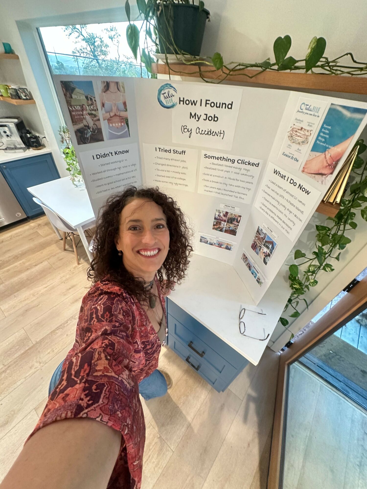 Woman taking a selfie in front of a display board with information and images, indoors with wooden flooring and a window.