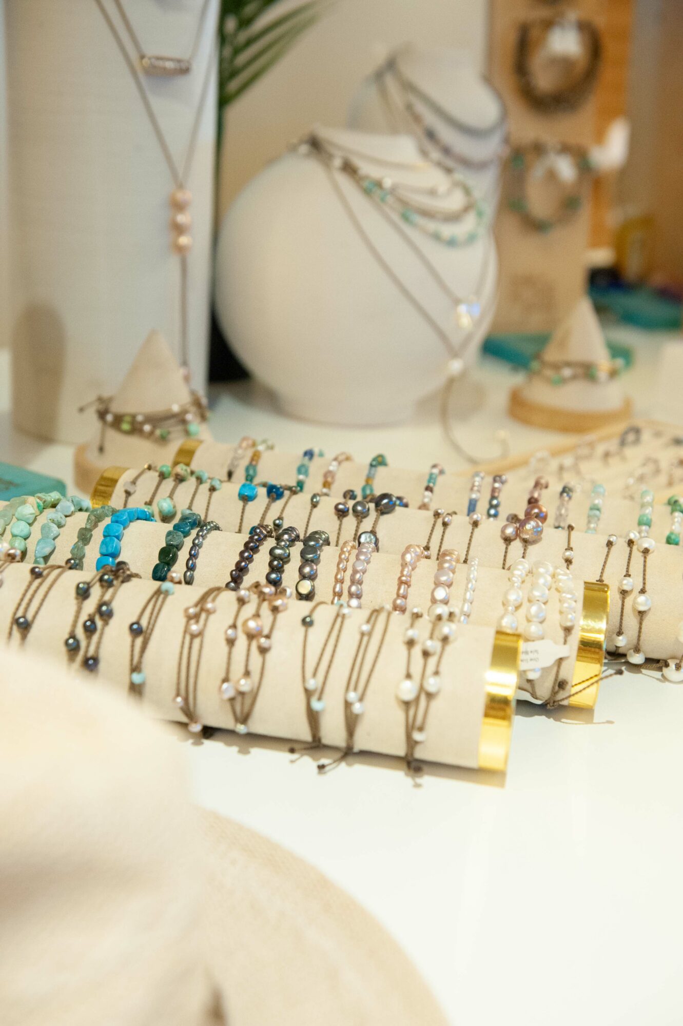 Display of various necklaces and jewelry on a white stand with a blurred background of jewelry pieces and decor.