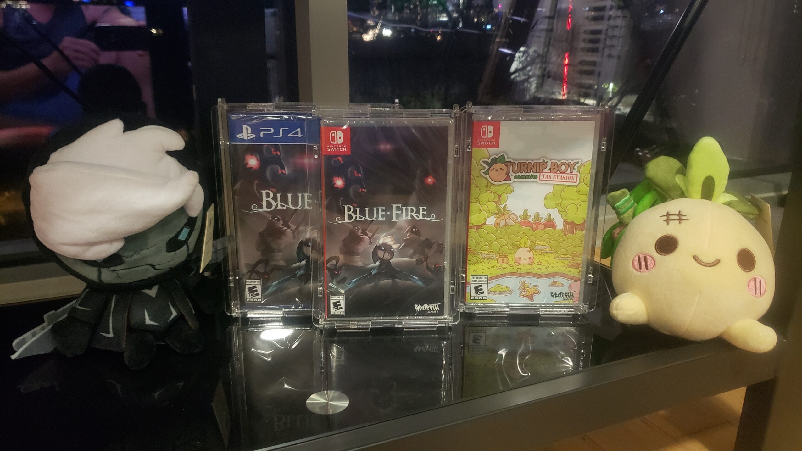 Two PlayStation 4 game cases, a plush toy with green ears, and a white plush figure on a windowsill at night.