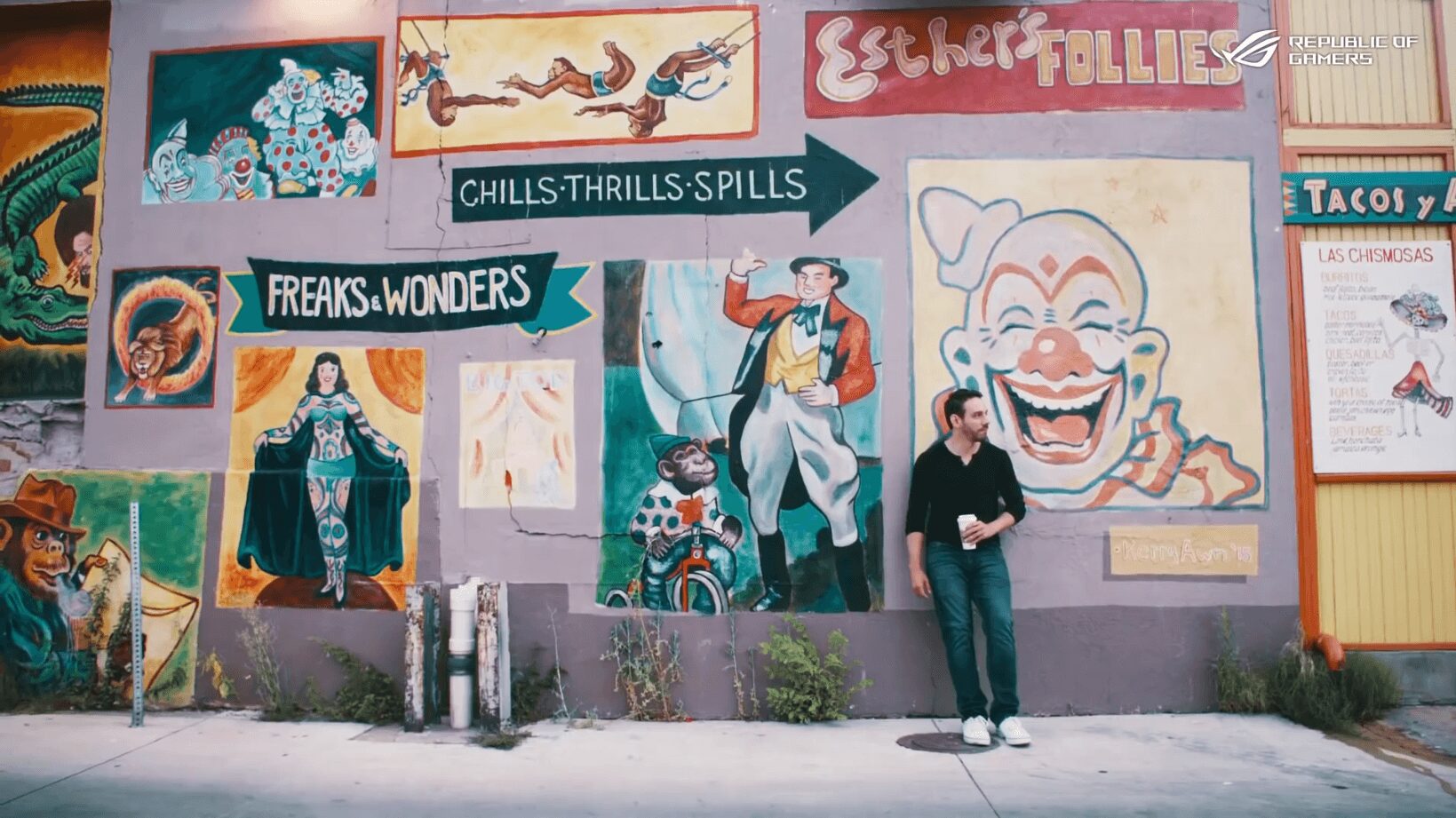 Two people stand in front of a colorful mural with clown, circus, and thrill ride images, and directional signs. Word count: 24.