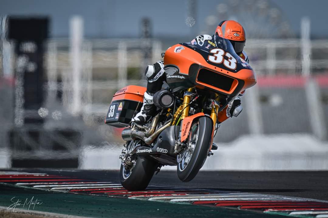 Motorcycle racer in orange and black gear leaning into a turn on a race track.
