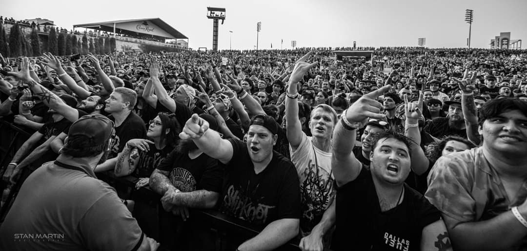 Large crowd of people at a concert or event, raising hands and cheering outdoors, black and white image.