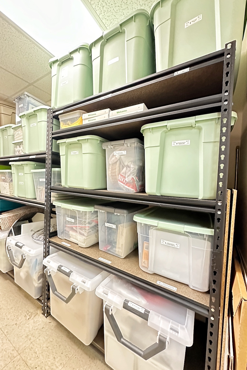 Shelves filled with green and clear storage bins containing various items, in a storage room.