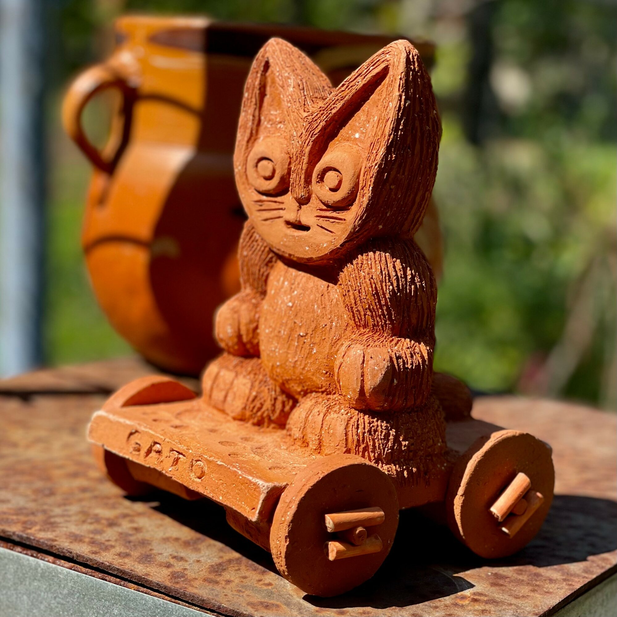 Wooden rabbit figurine on wheels with carved details, placed outdoors on a wooden surface, with a blurred background of greenery.