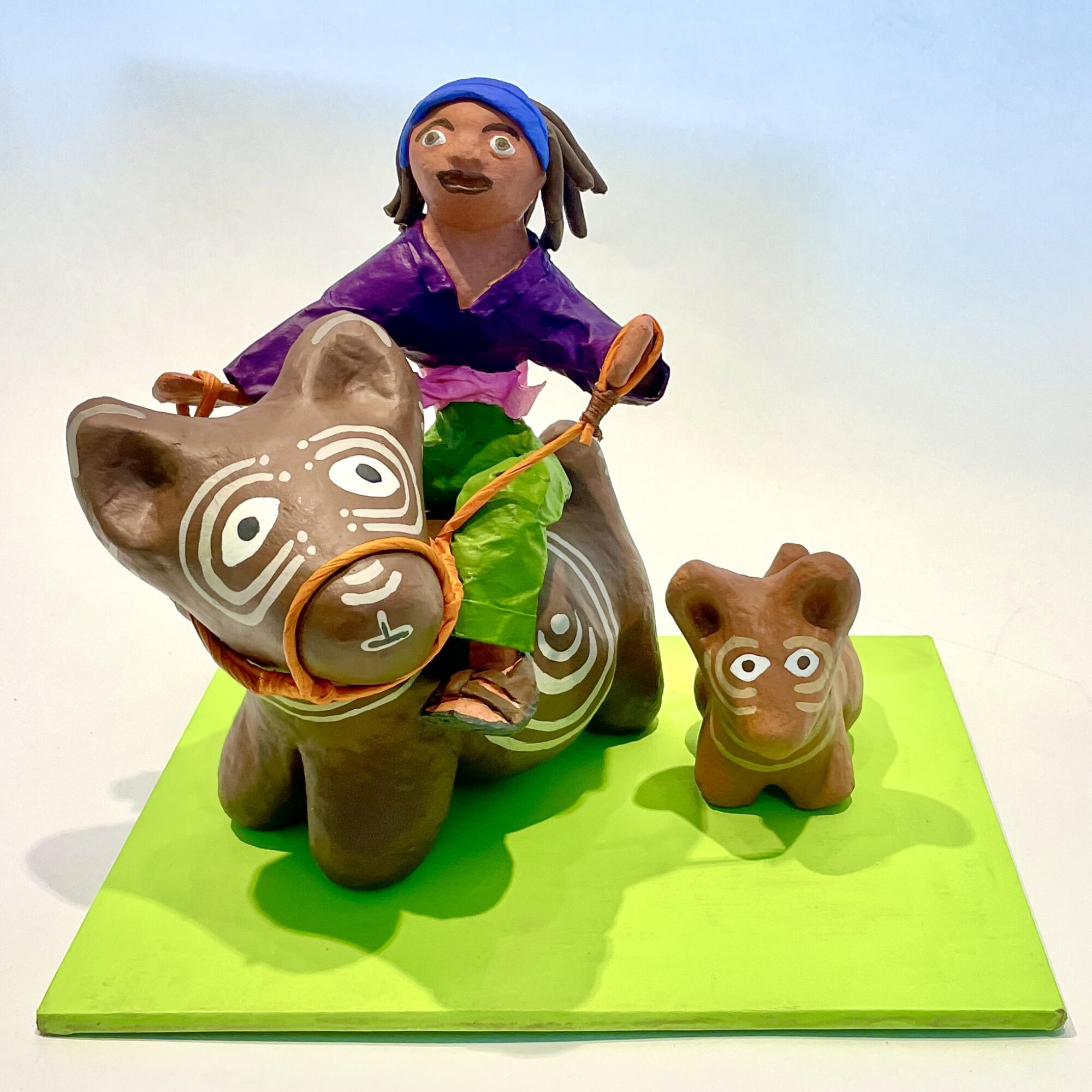 Figurines of a girl riding a large animal and a small animal, both with painted faces, on a green base.