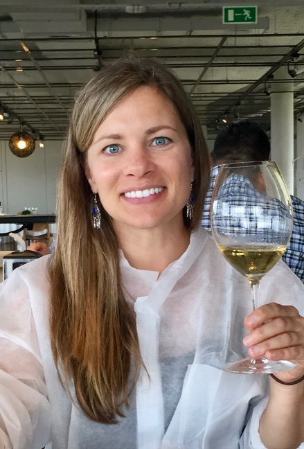 Woman with long hair holding a glass of white wine, smiling, in a restaurant setting.