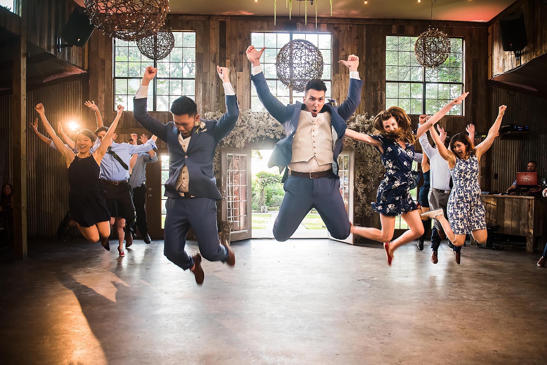 Group of people jumping and celebrating indoors with large windows and hanging spherical decorations.