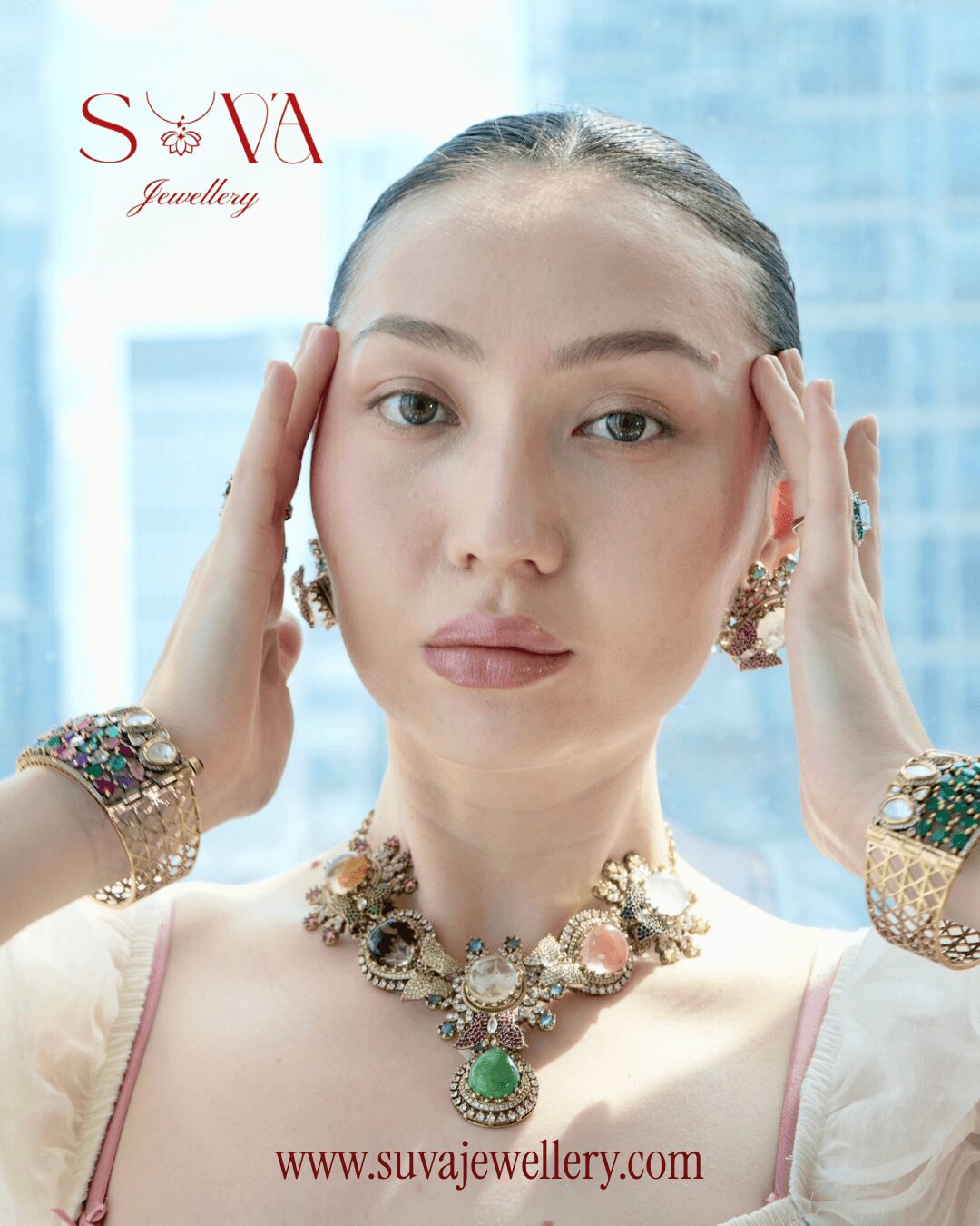 Young woman with jewelry, hands near face, cityscape background, wearing necklaces and earrings, looking at camera.