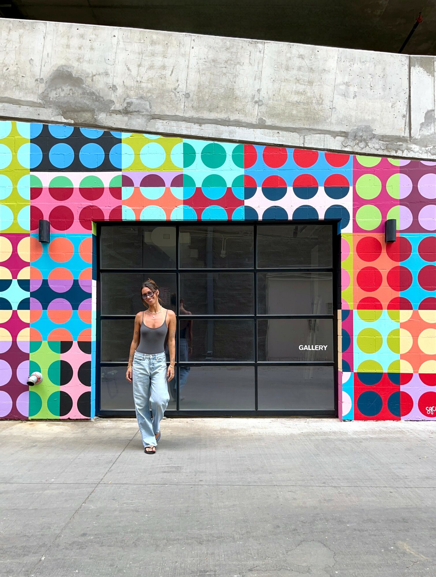 Person walking in front of a colorful, patterned wall with a black window and a small sign that says 'GALLERY'.