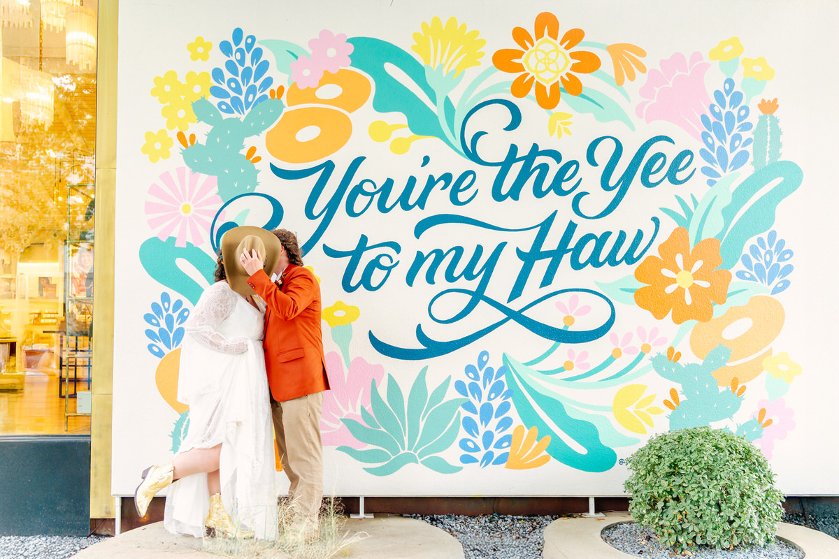 Two people hugging in front of a colorful floral sign that reads