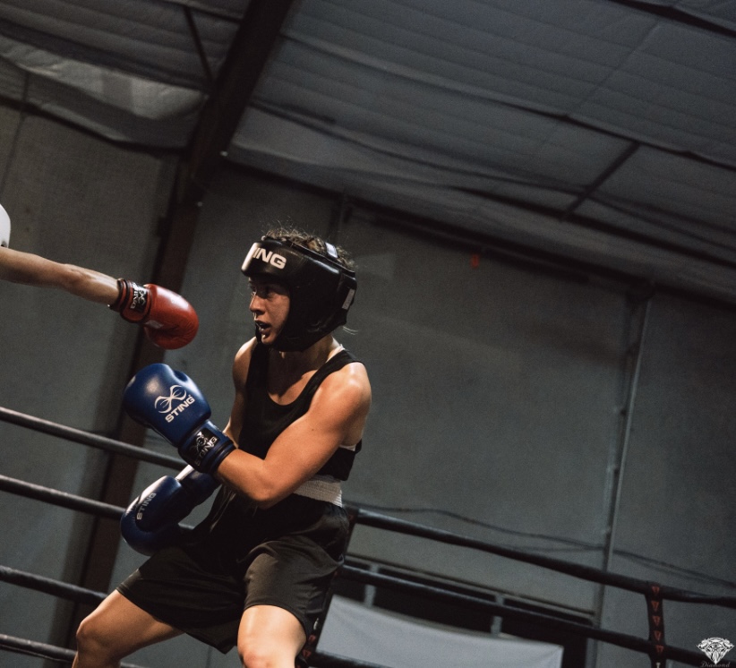 Female boxer in black gear and helmet throws a punch in a boxing ring.