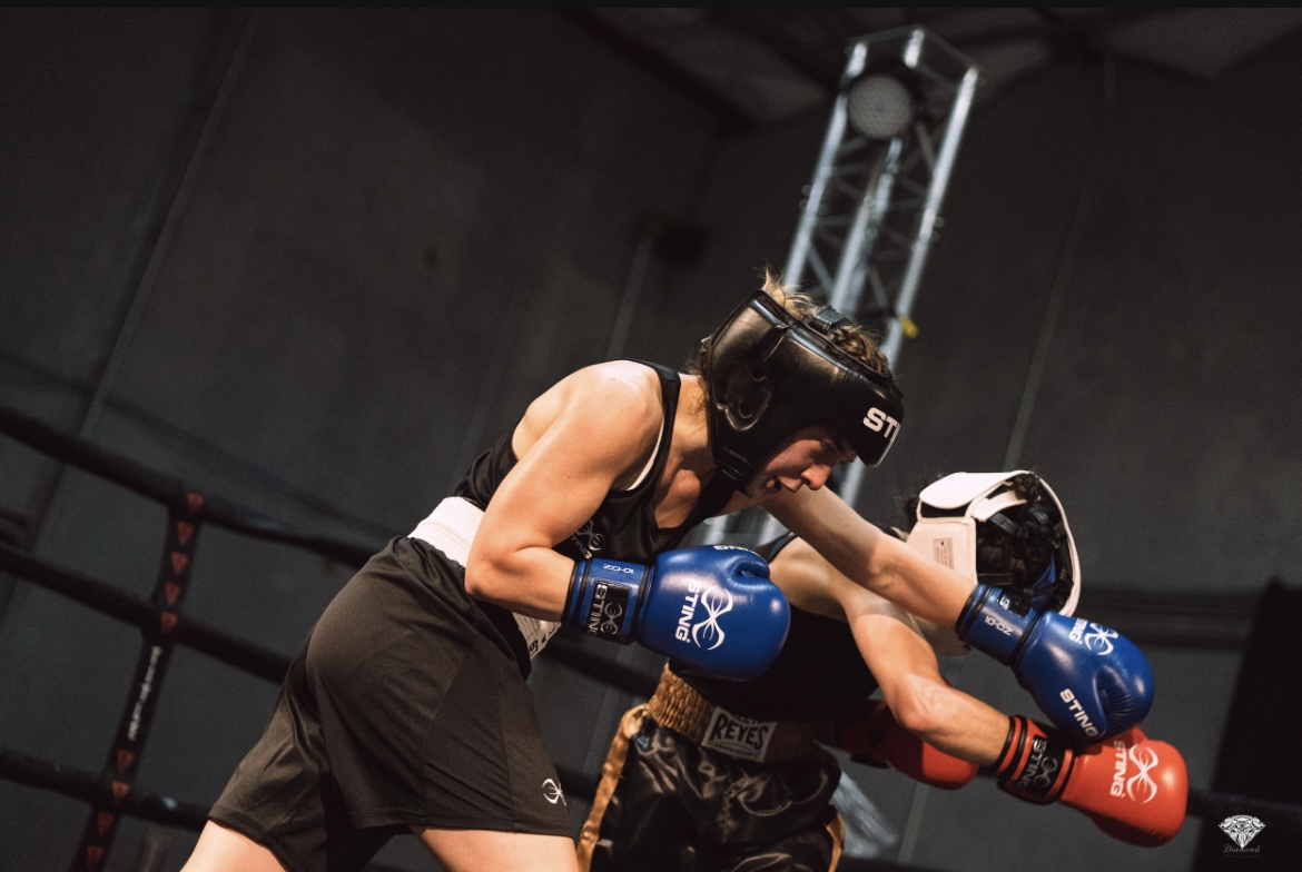 Two female boxers in a match, one delivering a punch to the other's face, wearing protective gear and gloves.