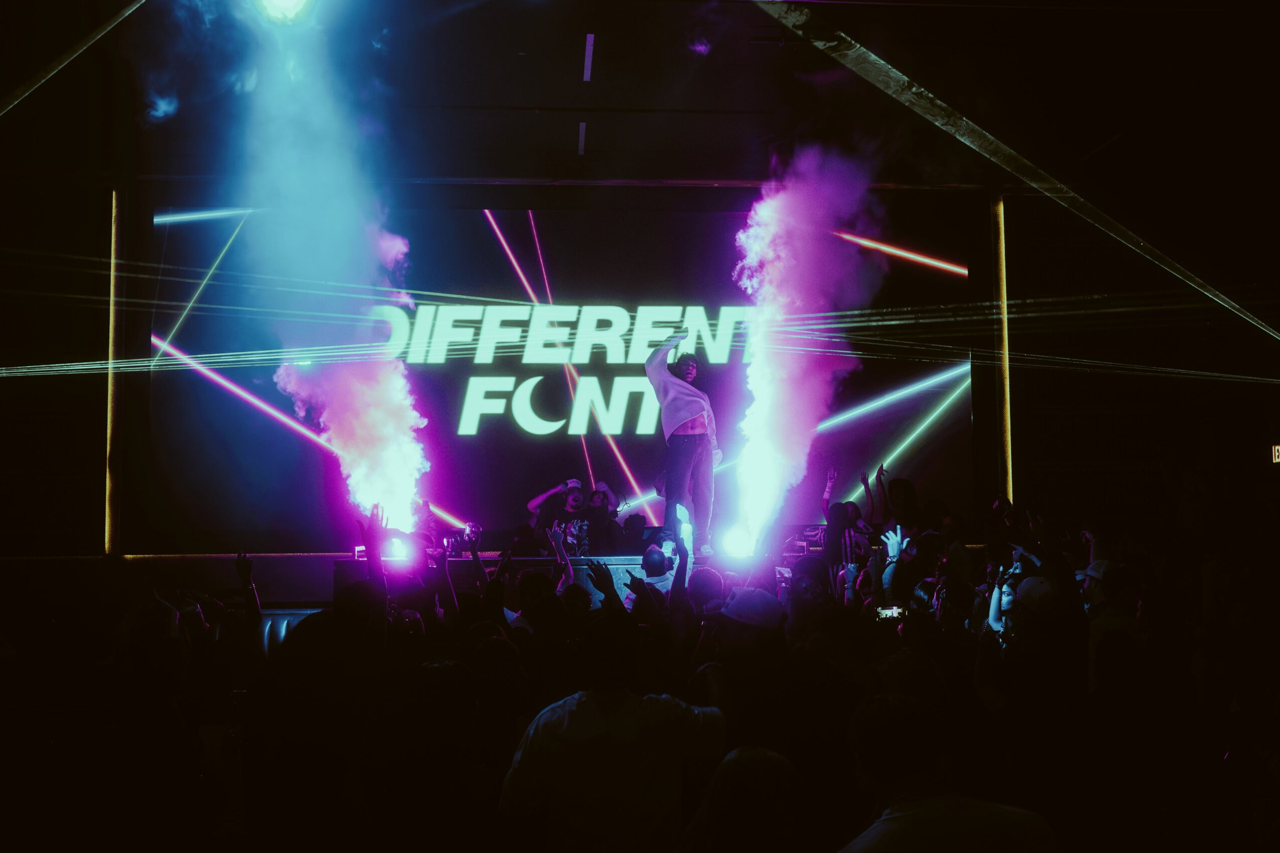 Stage with bright neon lights, smoke effects, and a large screen displaying 'DIFFERENT FCN' in a dark setting.