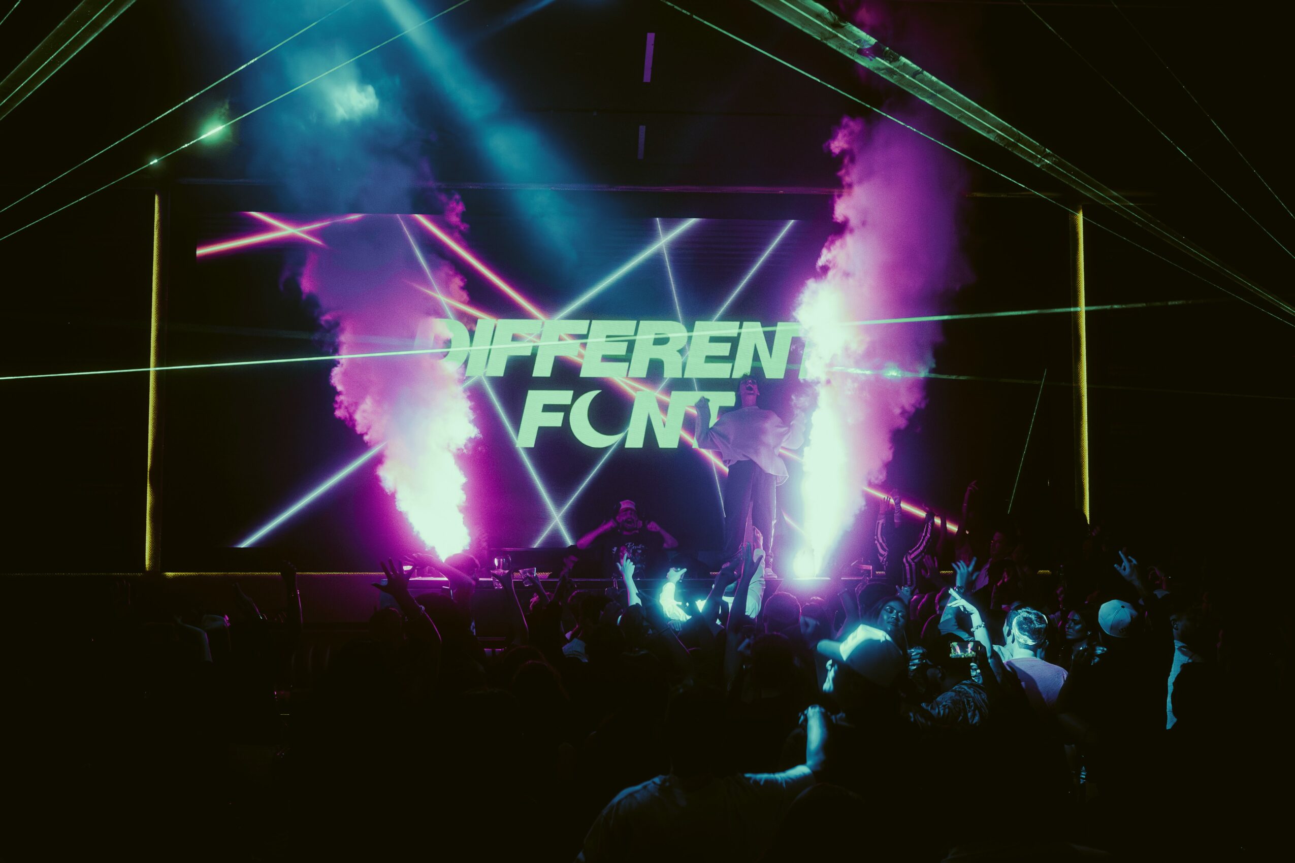 Stage with bright lights, smoke, and a screen displaying 'DIFFERENT FIGHT' in a dark concert setting.