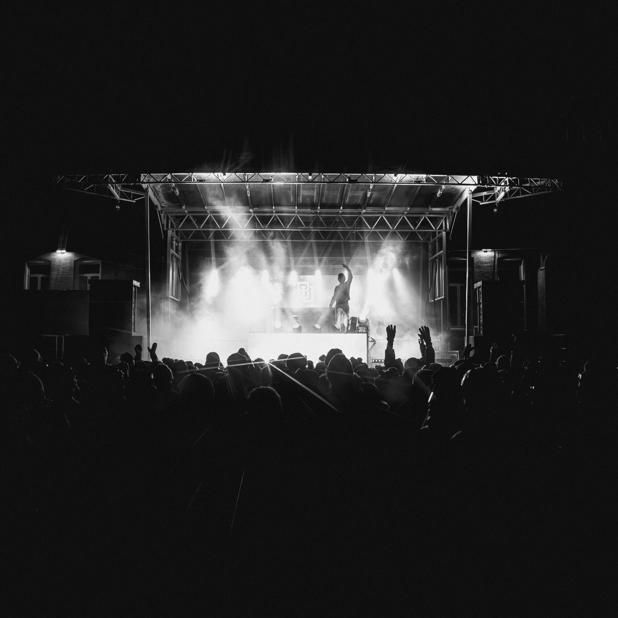 Concert stage with performer and bright lights, audience silhouettes in foreground, black and white image.