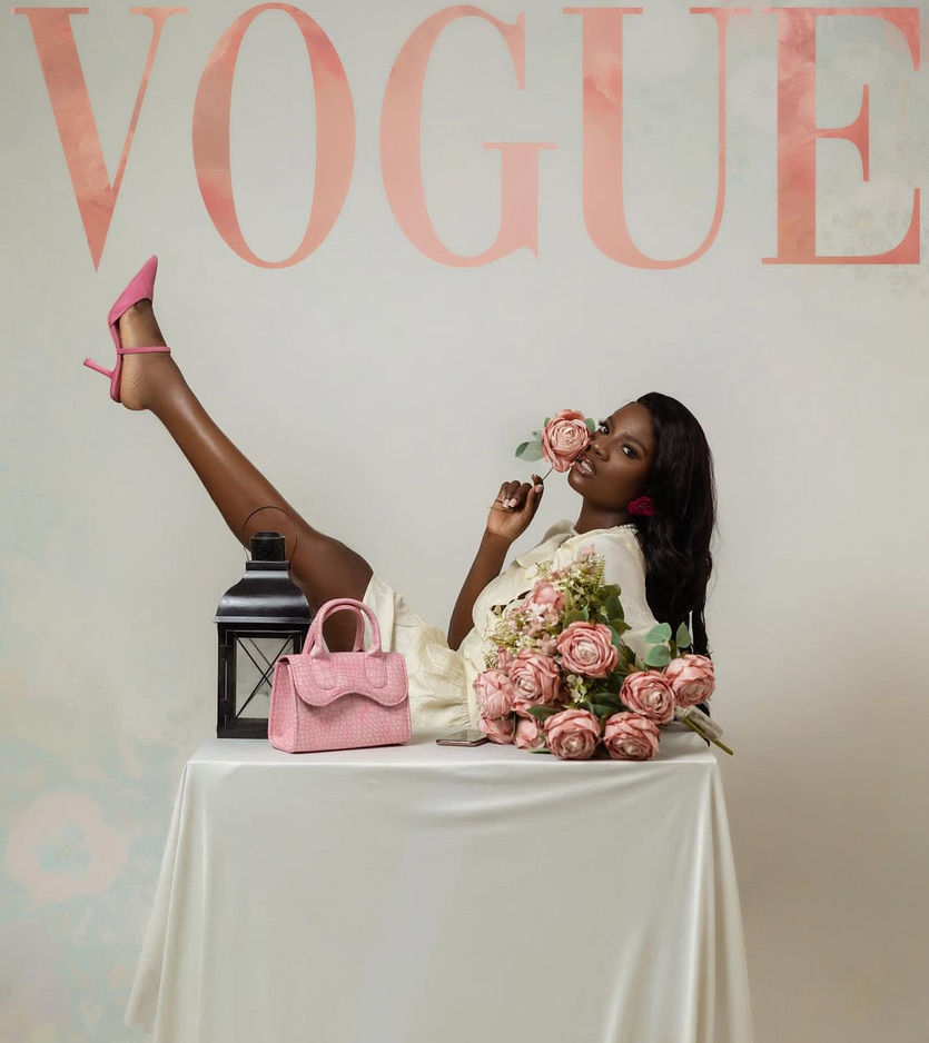 Woman sitting at a table with pink roses, a pink handbag, and a black lantern, holding a rose near her face.