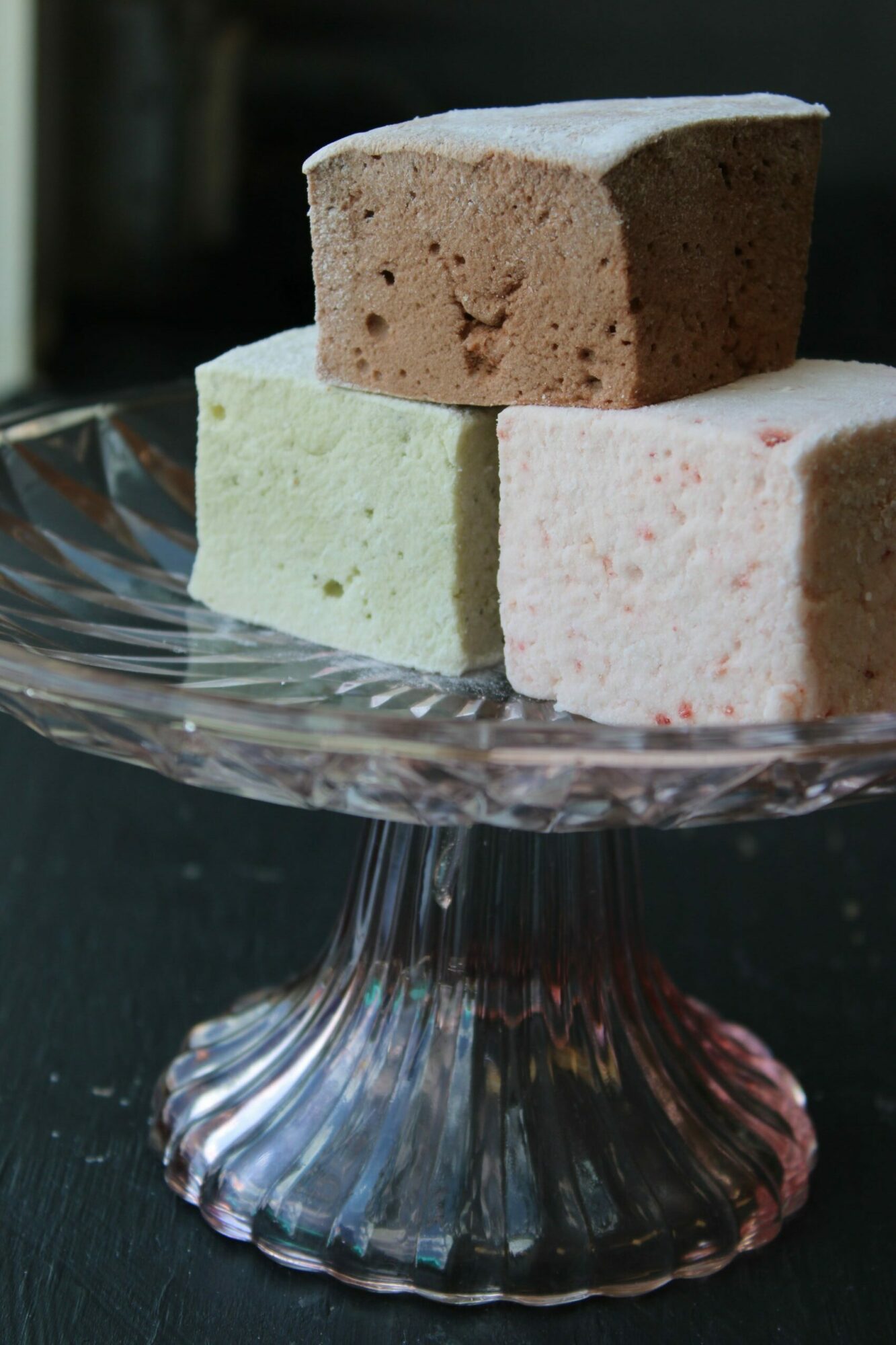 Four colorful square blocks on a glass dish, with a dark background, viewed sideways.