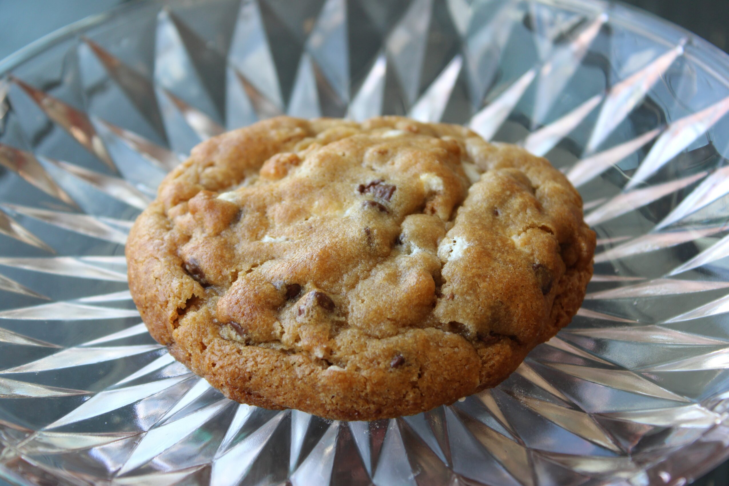 Chocolate chip cookie on a decorative glass plate, close-up view, with visible chocolate chunks.