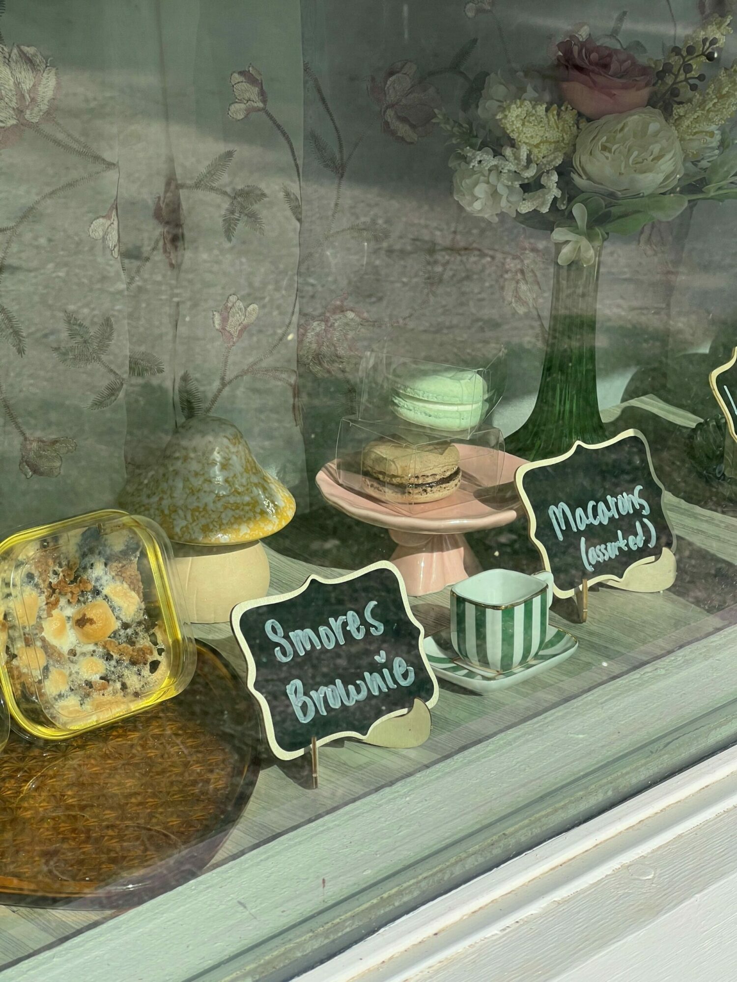 Cookies with black and white labels reading 'Sweets & Baking' on a windowsill, with flowers and potted plants in the background.