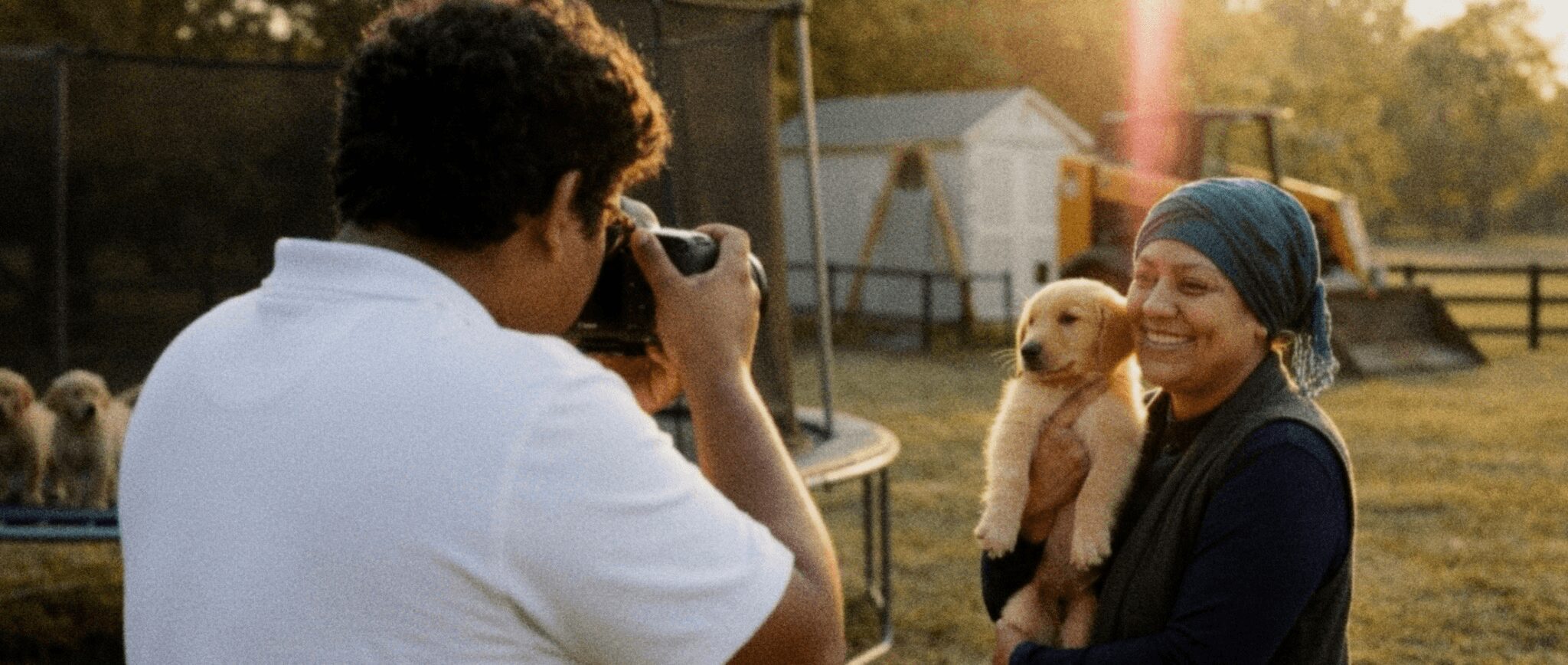 Person taking photo of woman holding a puppy outdoors during sunset.