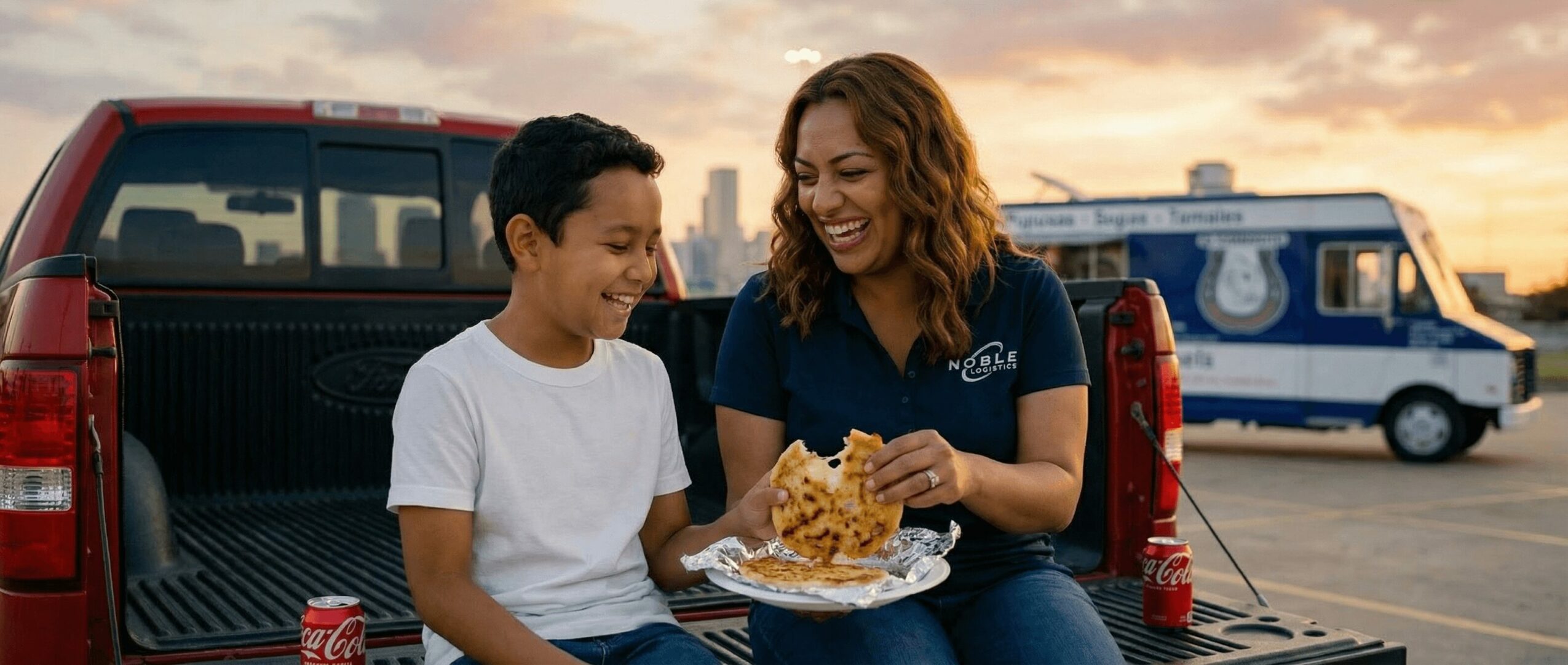Woman and boy sitting on truck bed, sharing a slice of pizza outdoors during sunset.