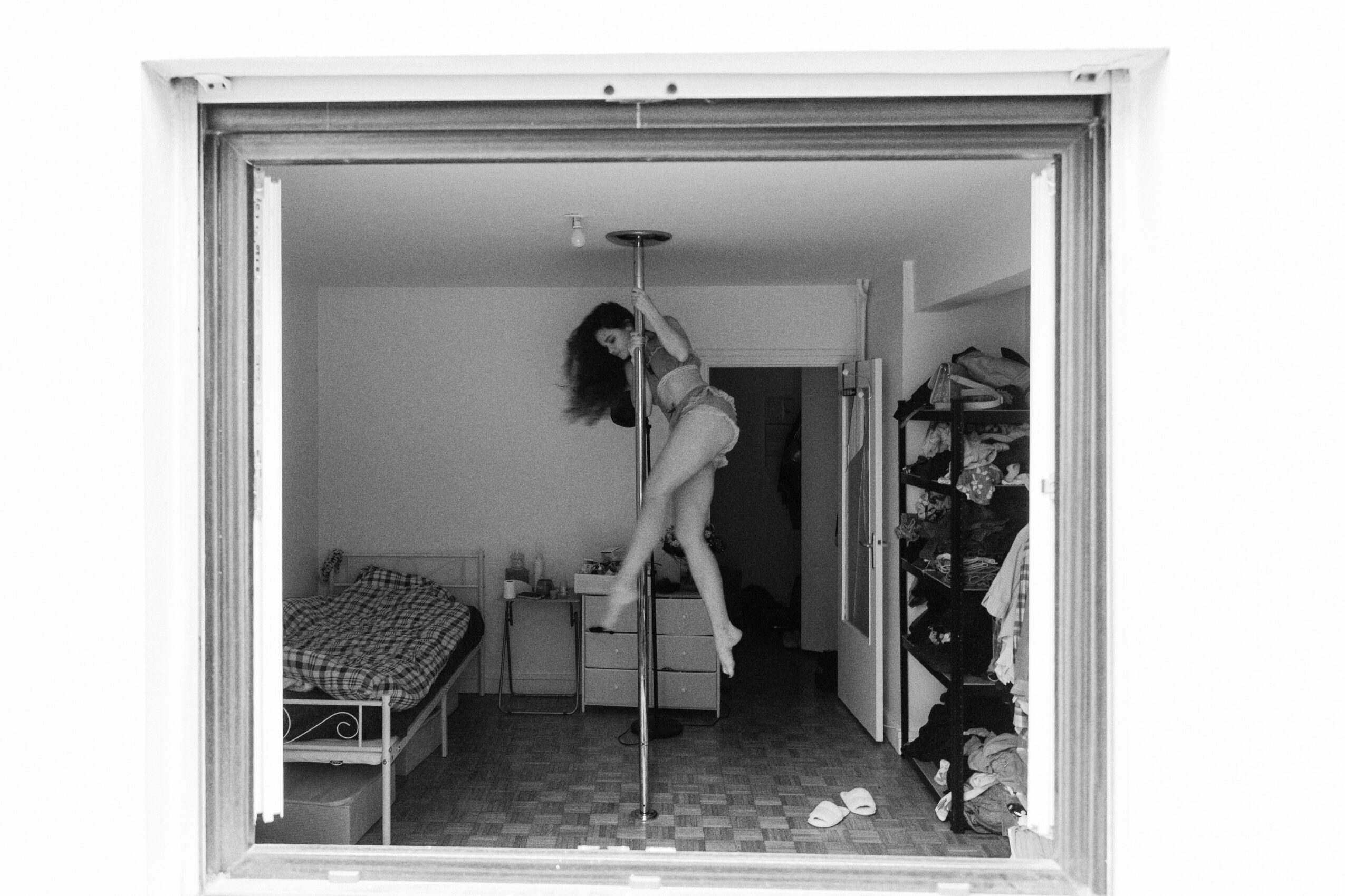 Person climbing a pole in a bedroom with a bed, open closet, and scattered clothes.