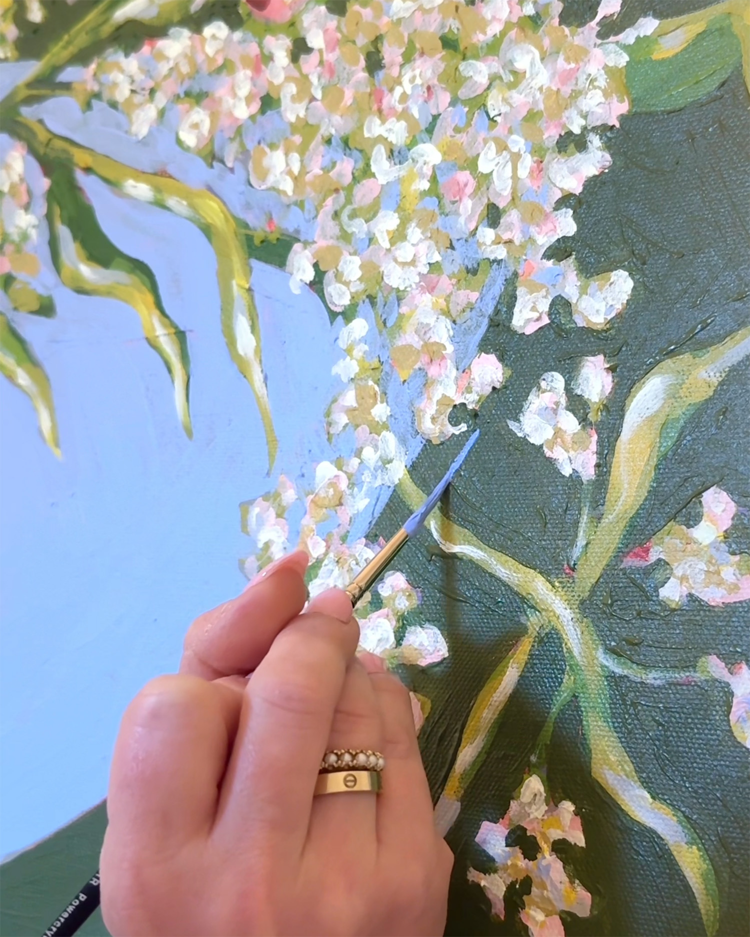 Person painting flowers with a brush on canvas, focusing on white and pink blossoms and green leaves.