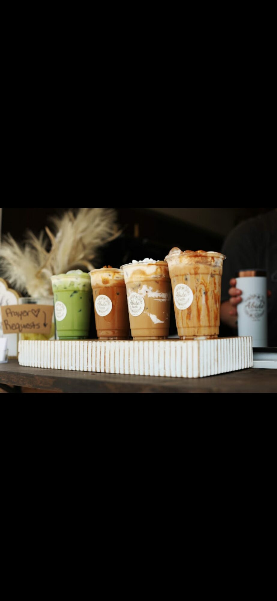 Four cups of coffee with whipped cream on a tray, with a small sign and a bottle nearby.