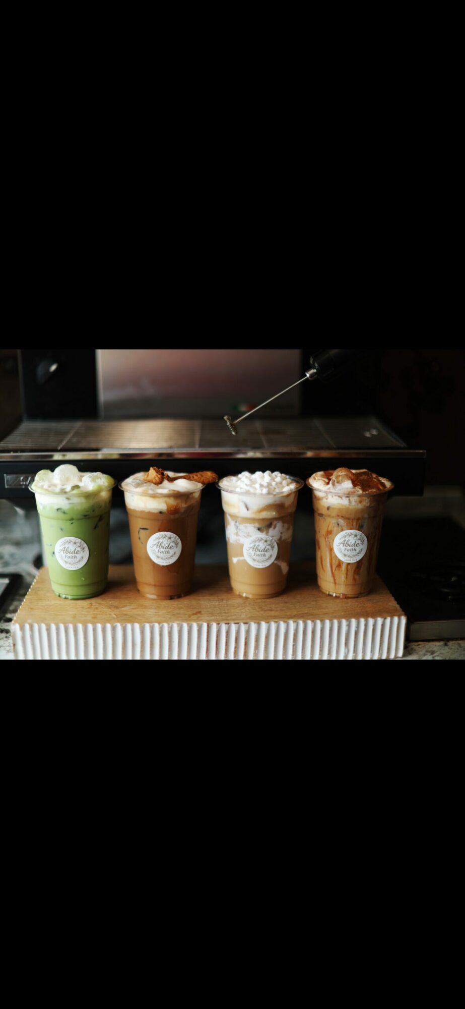 Four iced beverages with whipped cream and toppings on a wooden surface, with a dark background.