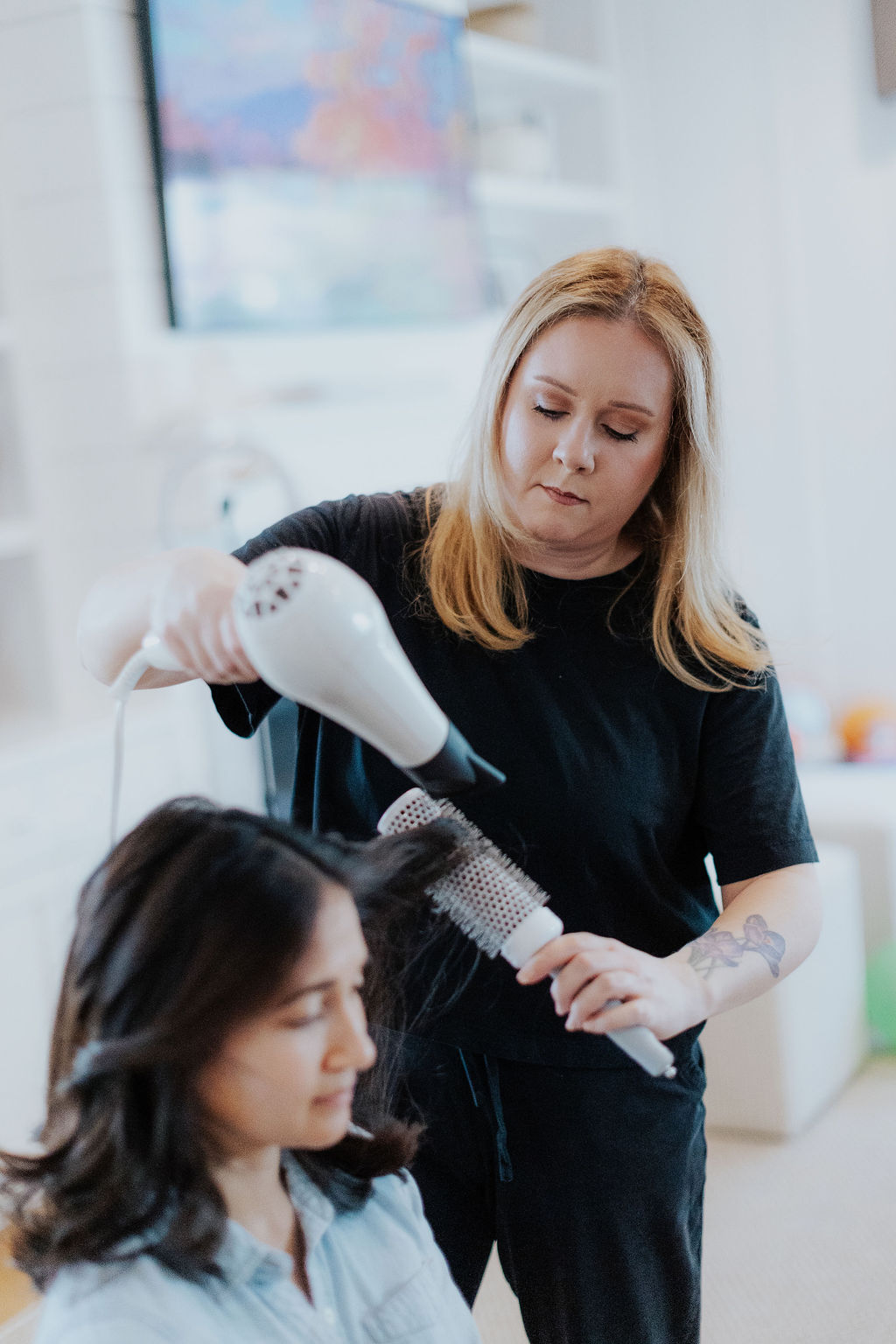Hairdresser dries a woman's hair with a blow dryer in a salon, with a blurred background.