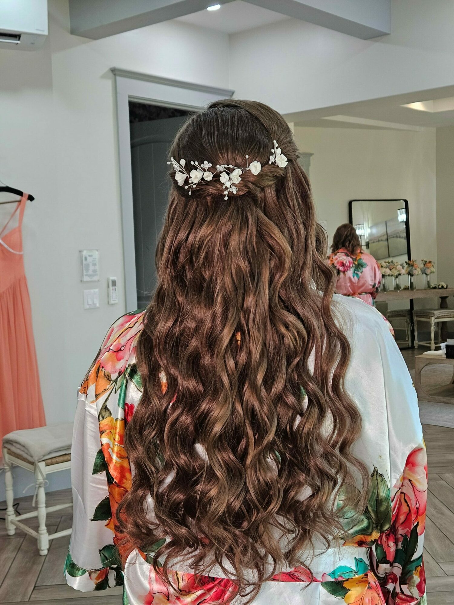 Back view of a woman with long, curly hair wearing a floral headband and colorful clothing in a room.