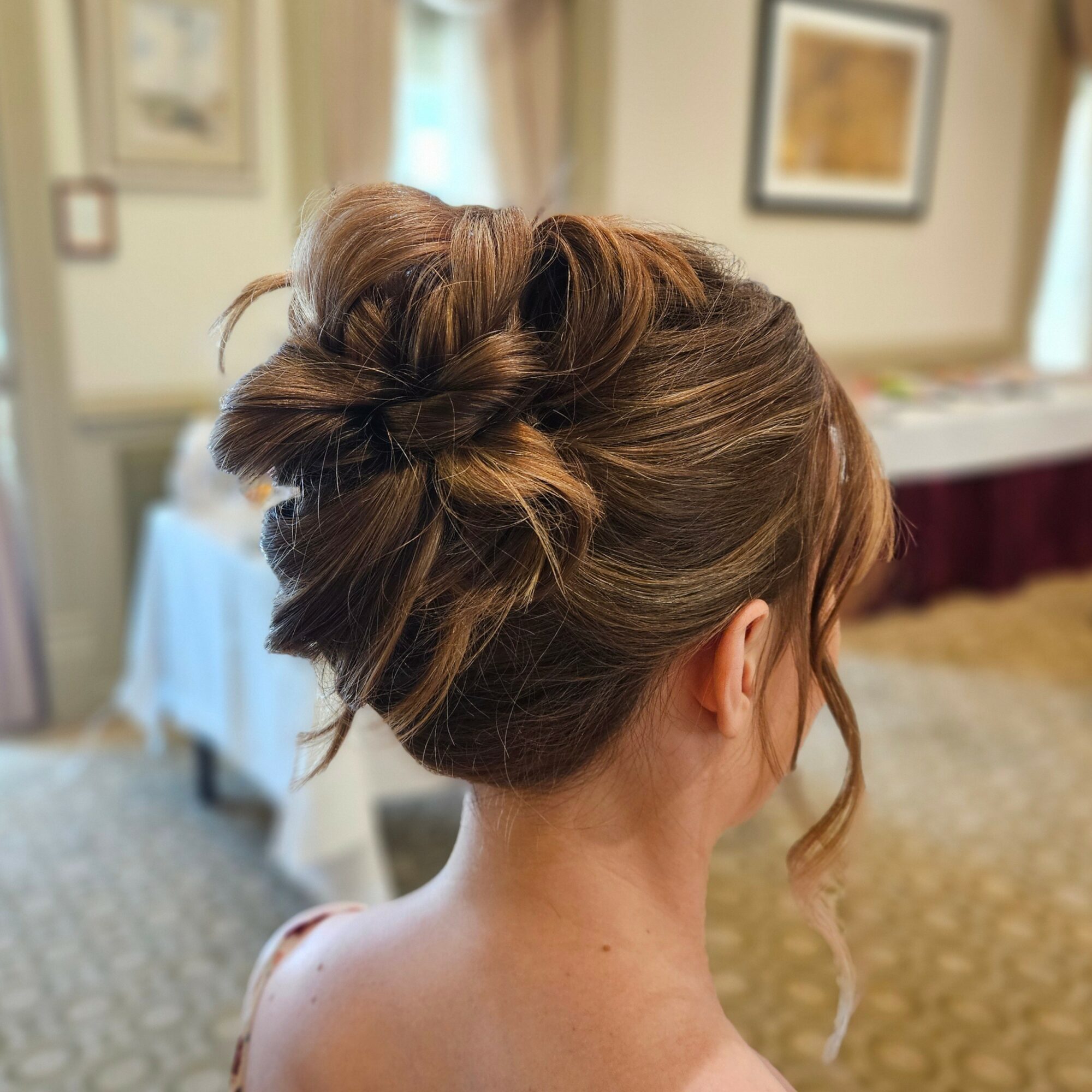 Back of a woman with an elegant updo hairstyle in a room with framed pictures and a table.