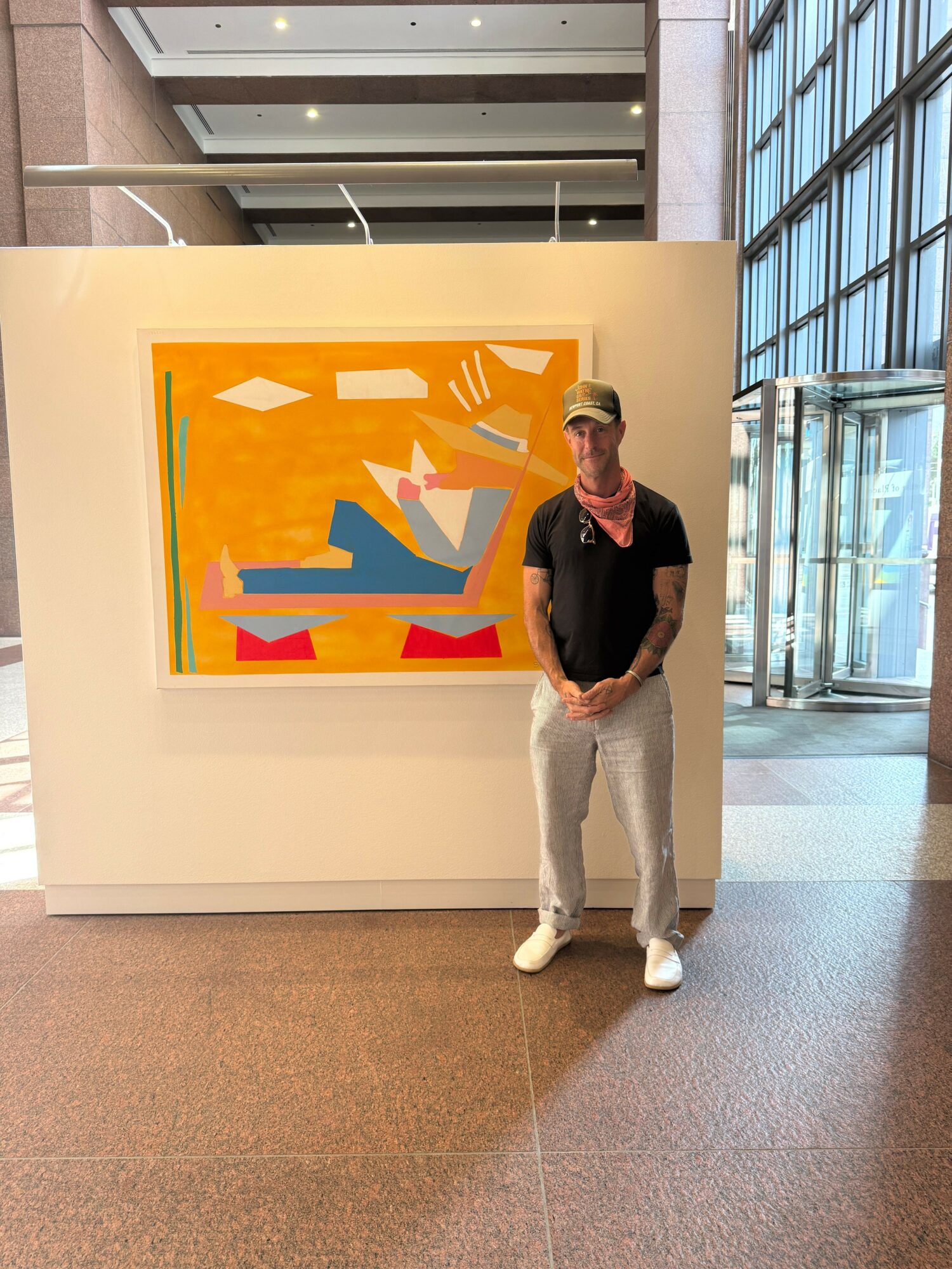 Person standing in front of colorful abstract painting in gallery, holding a phone, with glass ceiling and modern interior.