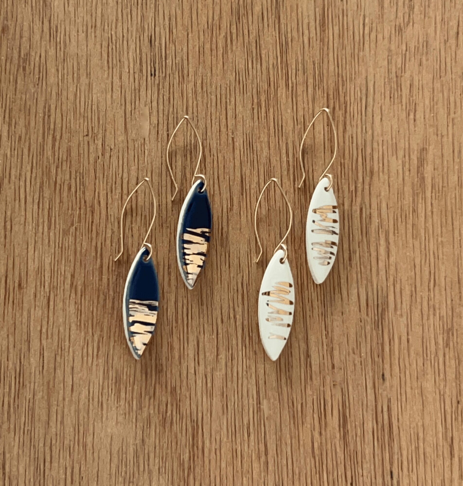 Two pairs of earrings, one pair with blue and silver design, the other with white and silver design, on a wooden surface.