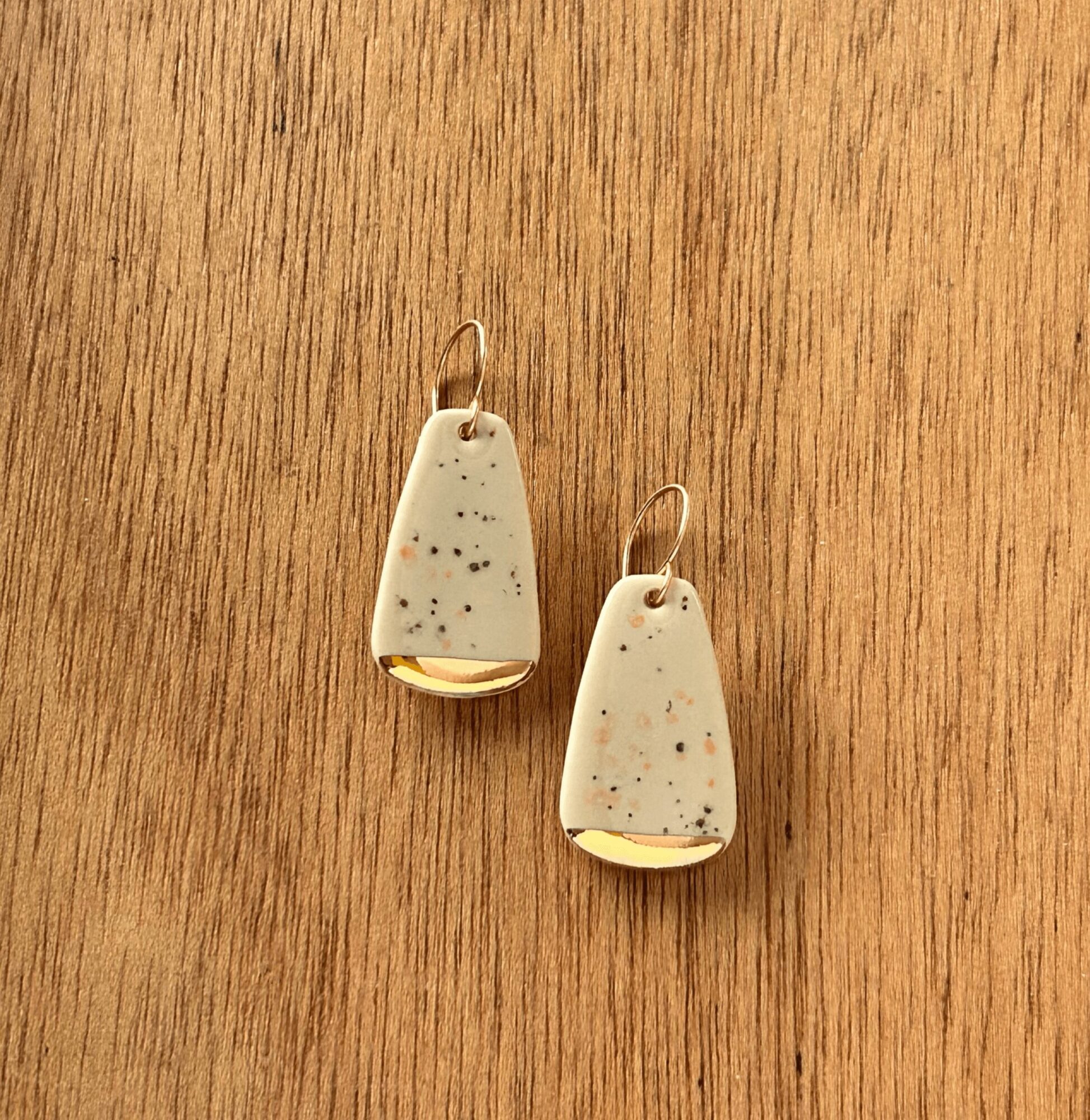 Pair of speckled earrings with gold accents on a wooden surface.