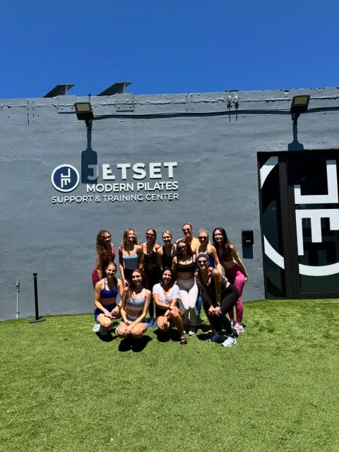 Group of people posing on a grassy area in front of a building with a sign that reads 'JETSET' and 'SUPPORTING THE BEST IN THE BUSINESS'.