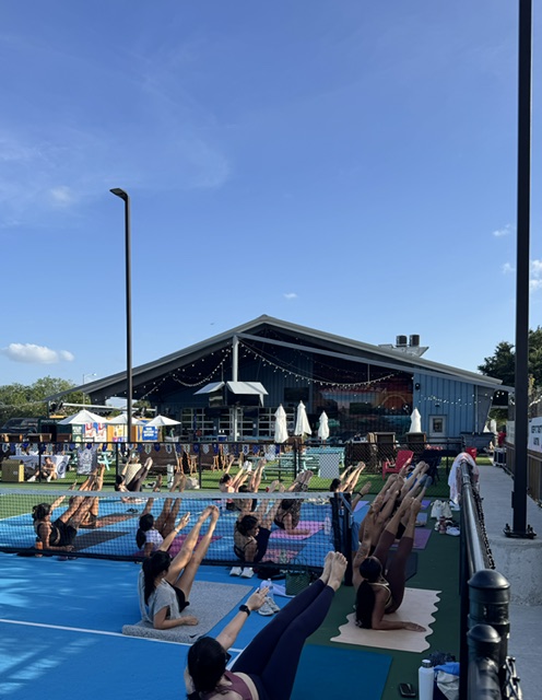 People practicing yoga outdoors near a building with a blue sky background.