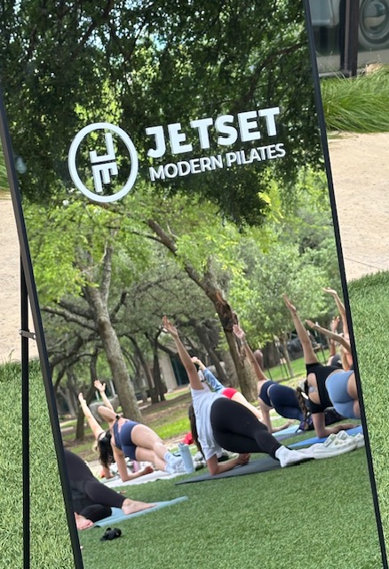 Group of people practicing yoga outdoors on mats in a park with trees and grass.