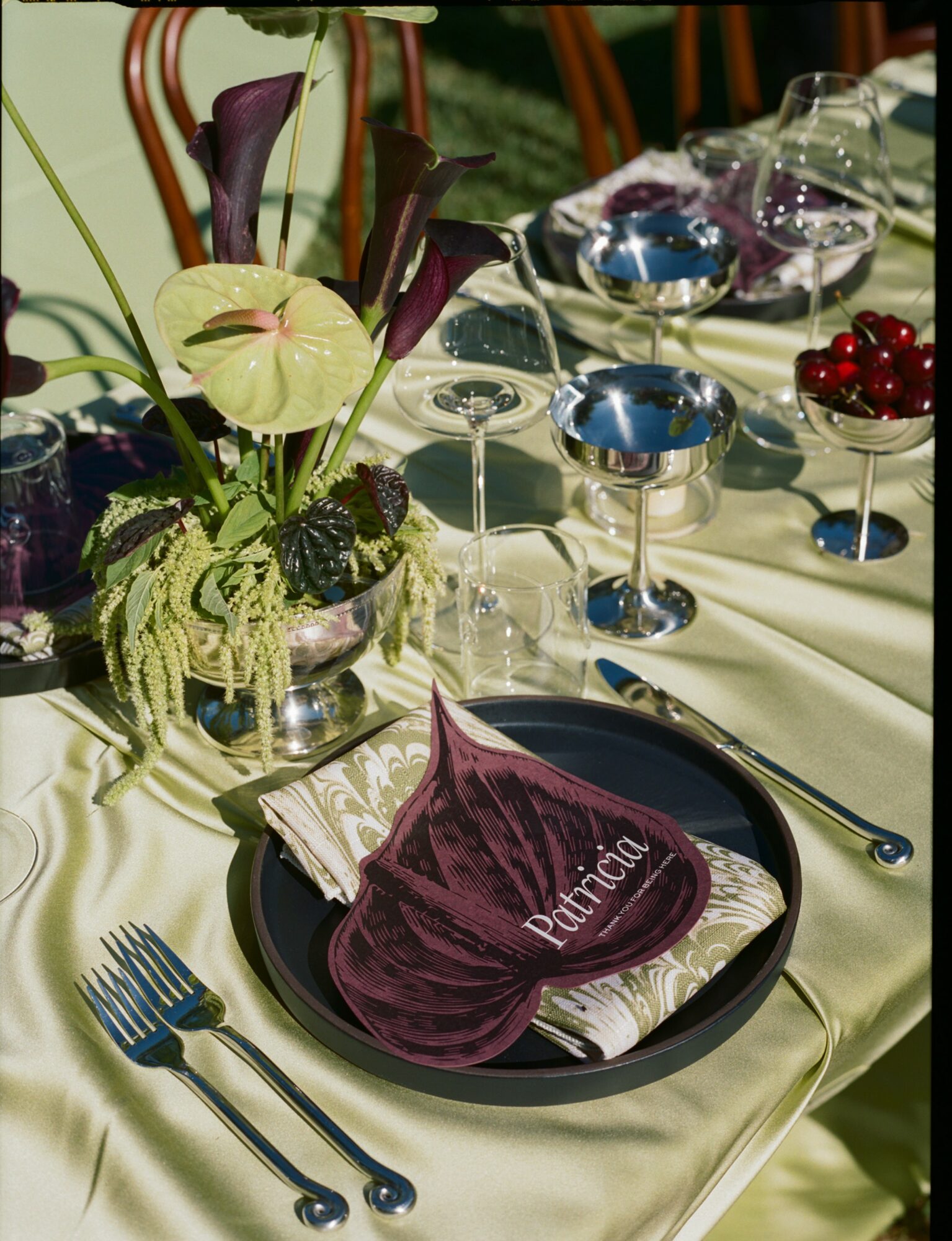 Table setting with a floral arrangement, black plate, purple napkin, and glassware, on a cream-colored tablecloth.