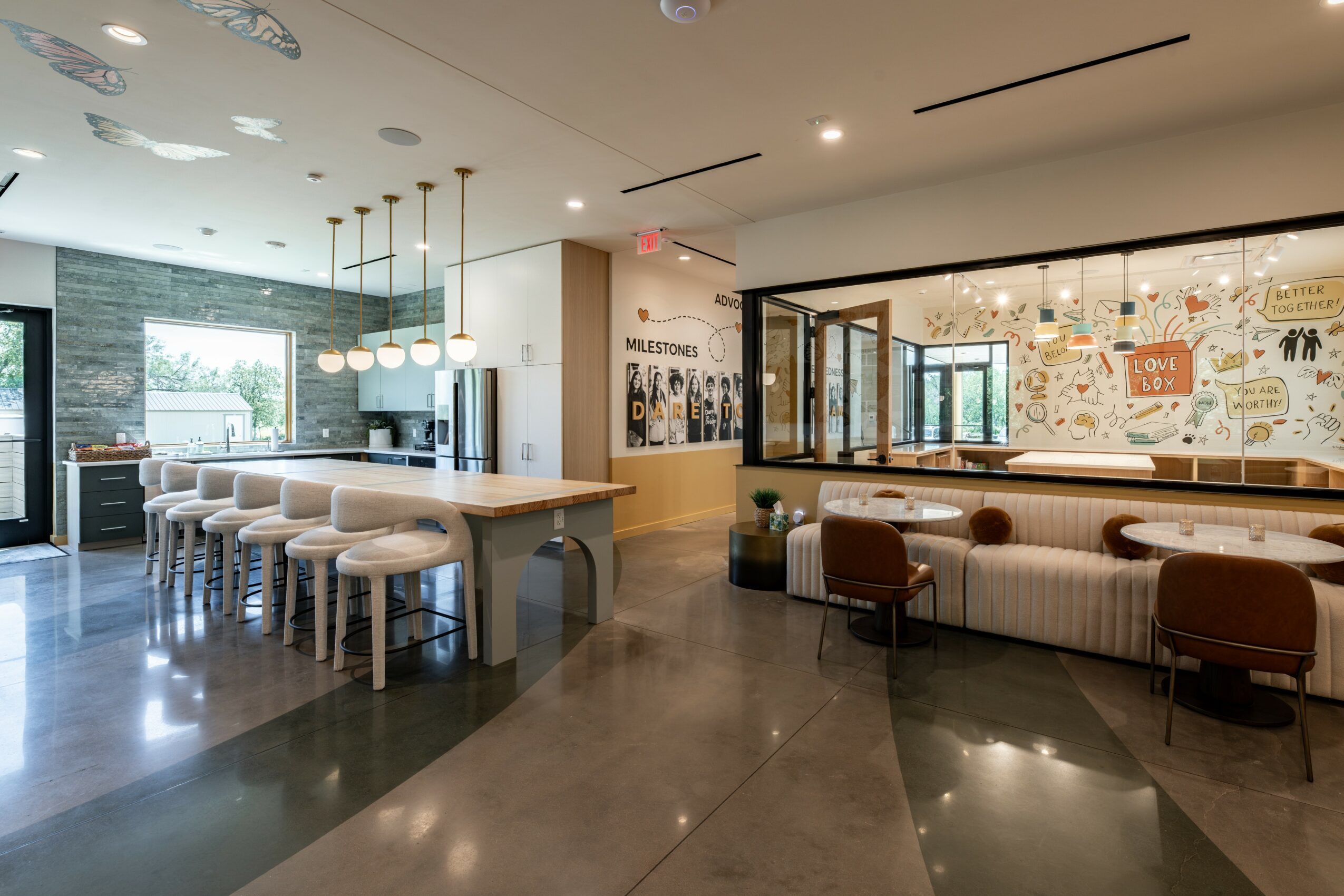 Modern cafe interior with a long table, bar stools, and a seating area with chairs and a window wall.