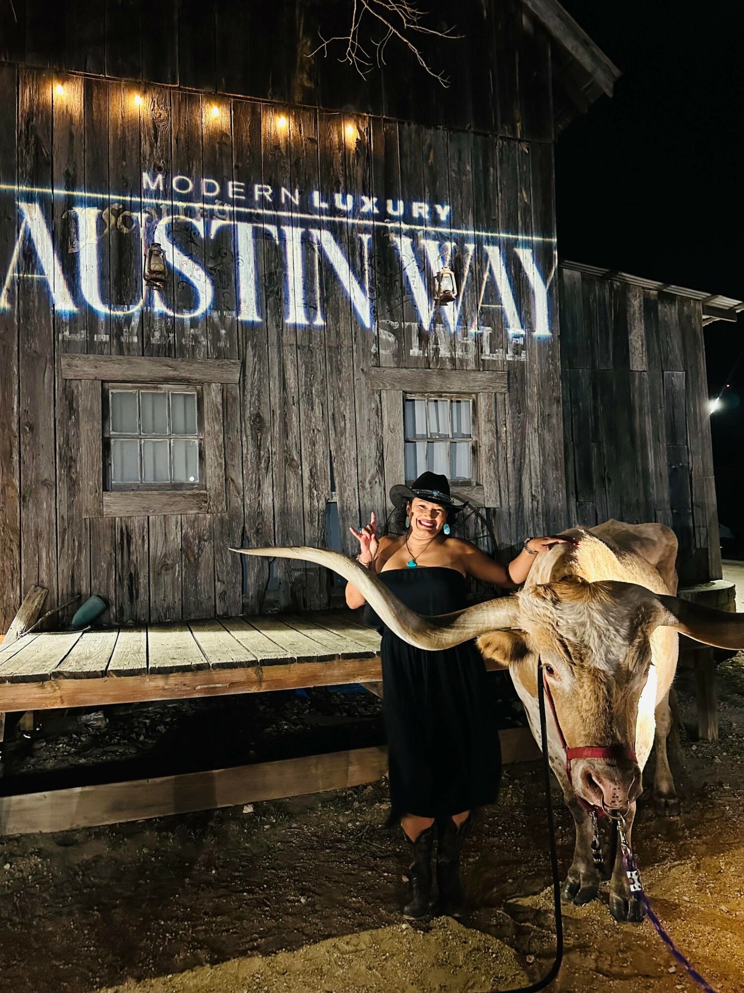 Person standing next to a cow in front of a wooden building with a sign reading 'AUSTIN WAY' and 'MODERN LUXURY'.