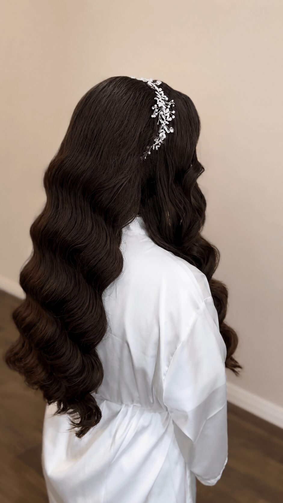 Side view of a woman with long, wavy dark hair wearing a white garment and a decorative hair accessory.