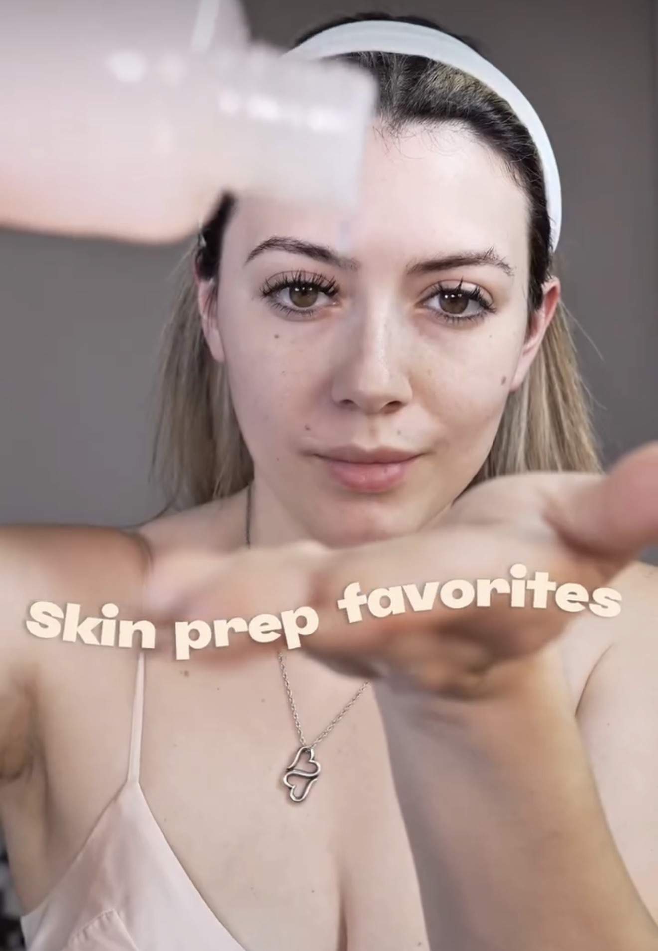 Young woman with headband holding skincare product, text overlay reads 'Skin prep favorites', neutral expression, gray background.
