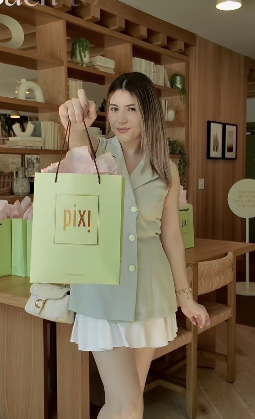 Young woman holding a Pixi shopping bag in a cozy store with wooden shelves and decor.