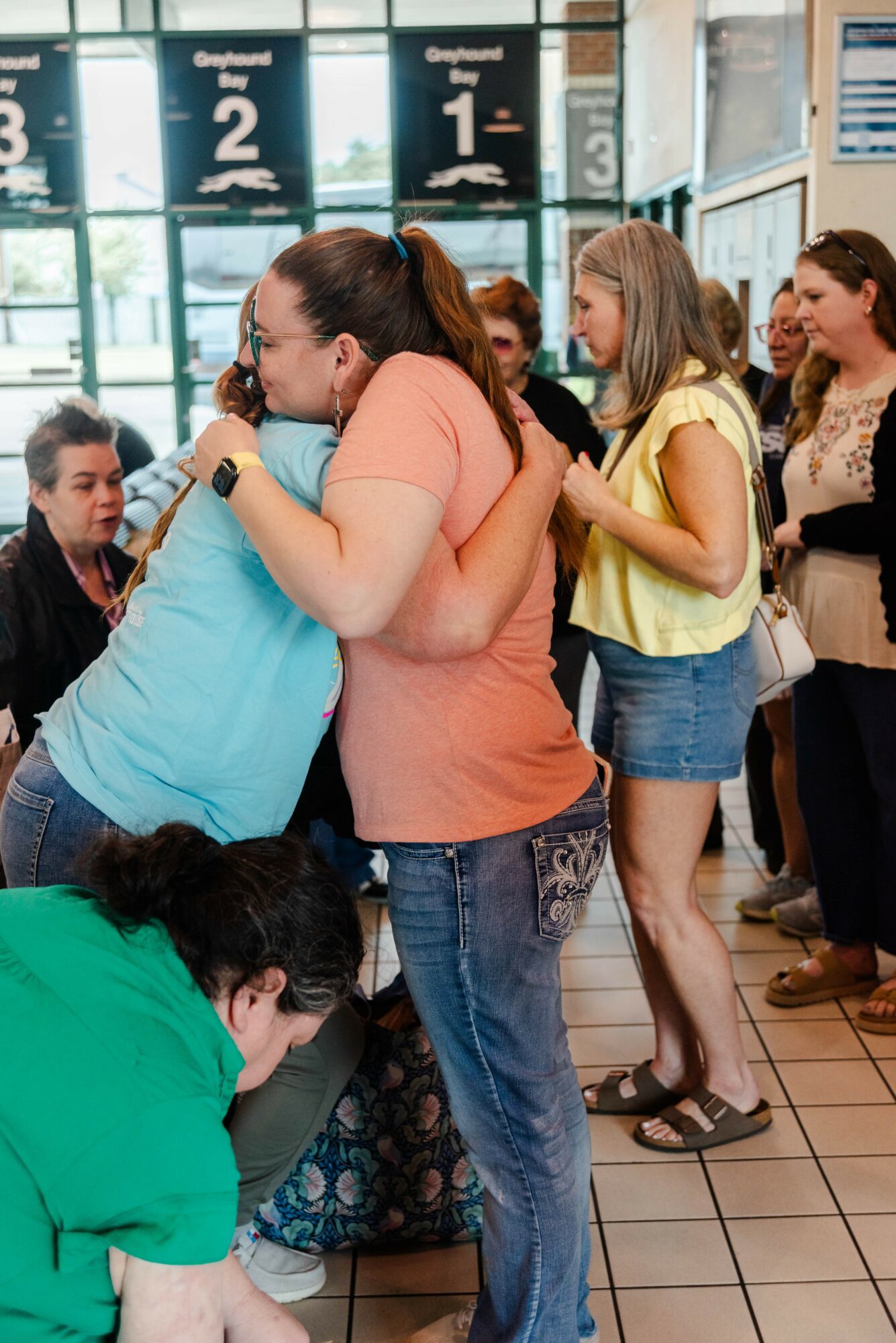 Group of people hugging inside a store, with signs displaying numbers in the background.