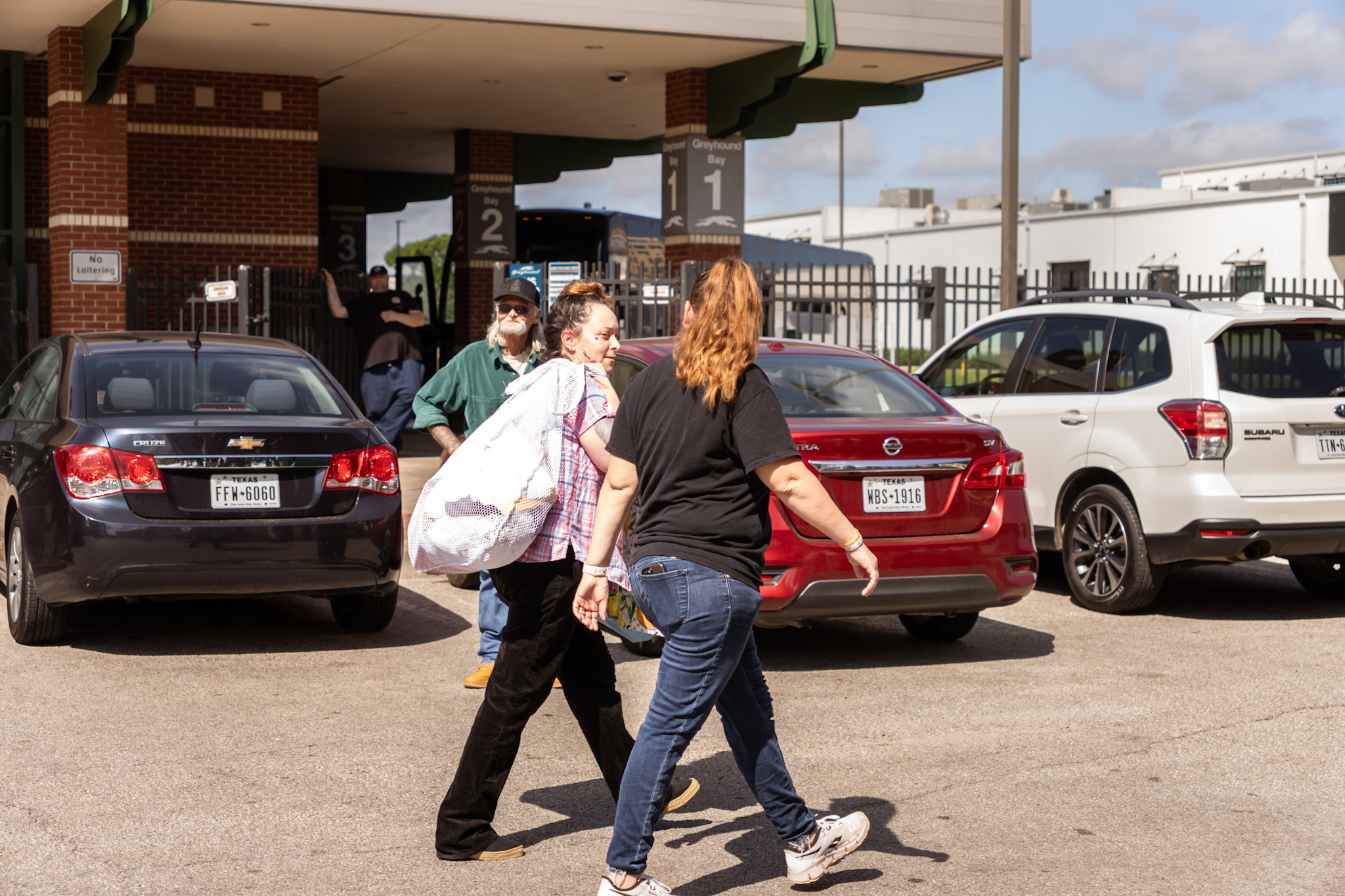 People walking in a parking lot with cars and a building in the background.