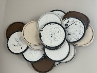 Collection of open and closed containers with white, brown, and black lids, some with visible contents, arranged on a surface.