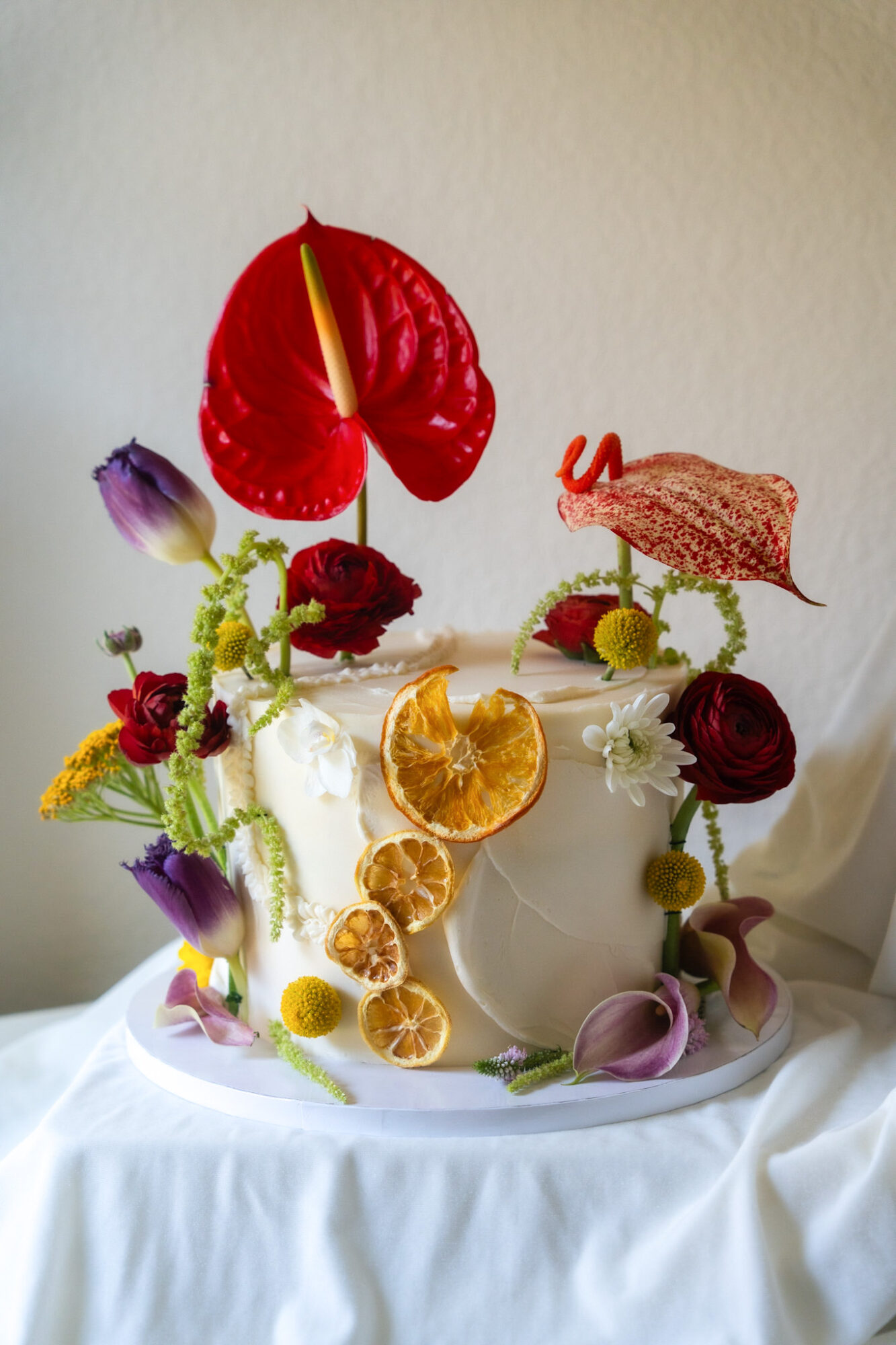 Decorative cake with flowers, dried citrus slices, and colorful elements on a white surface.