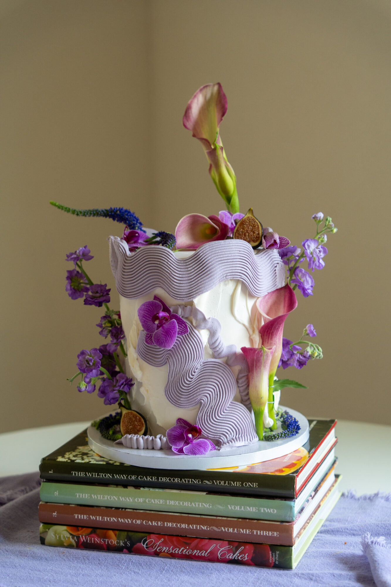 Decorative cake with flowers and fruits on top, placed on a stack of books, against a plain background.