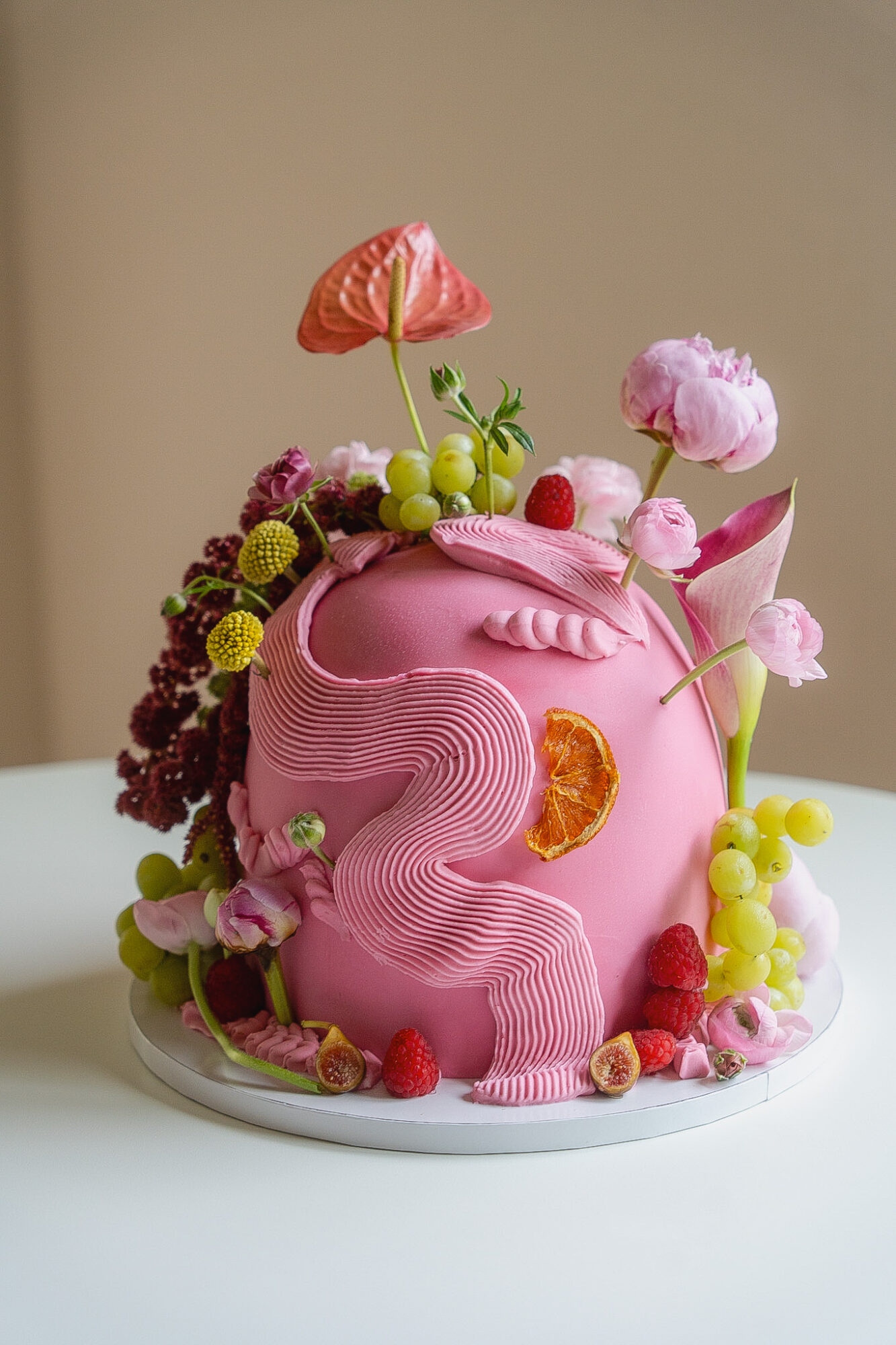 Pink birthday cake decorated with flowers, grapes, and fruit, featuring a large number 3 on the side.